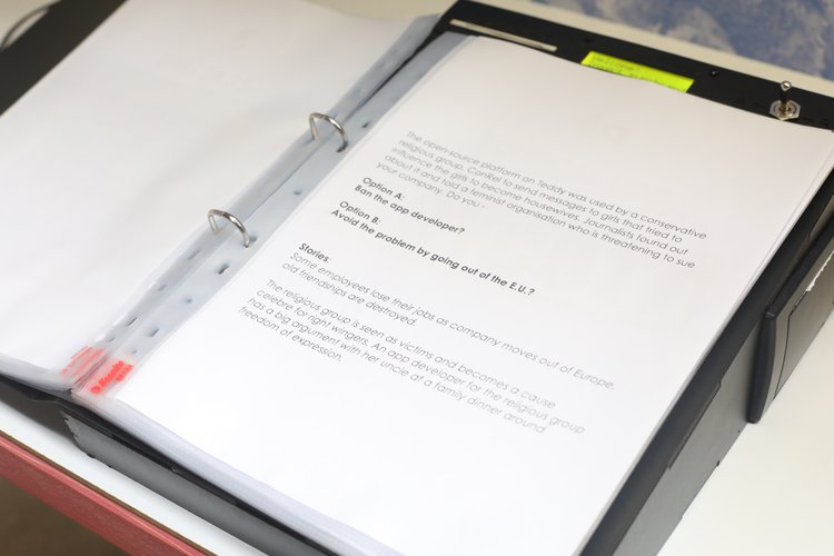 Operatorās manual page displayed in a binder, presenting a dilemma scenario where participants choose option A or B via a physical switch.