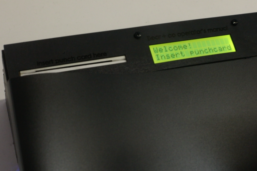 Close-up of the stationās LCD screen prompting āWelcome! Insert Punchcard,ā guiding participants through the sign-in interaction.